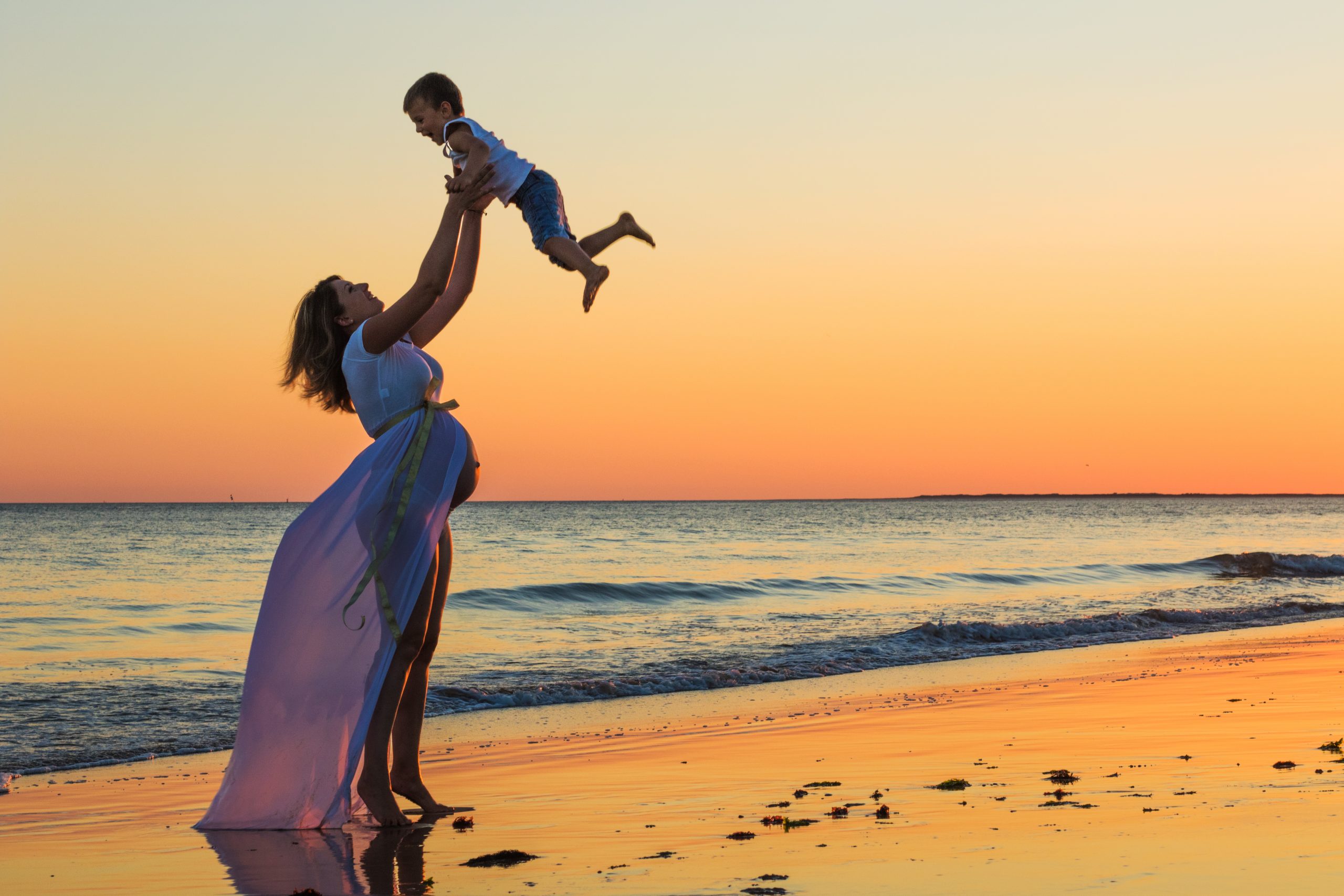 Femme enceinte portant son enfant face au coucher du soleil