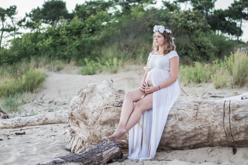 Femme enceinte portant une robe blanche, assise sur un tronc d'arbre