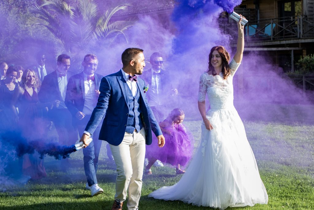 Mariés tenant des fumigènes bleus et violets devant leurs invités à Cognac